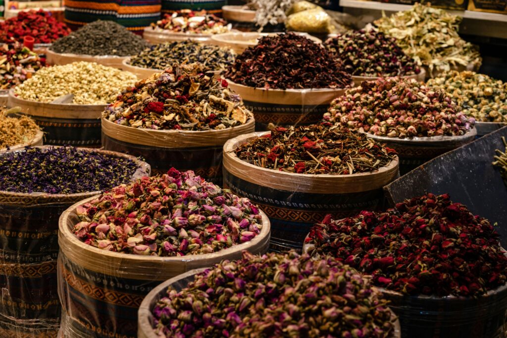 A colorful display of dried spices and herbs in barrels at a bustling market.